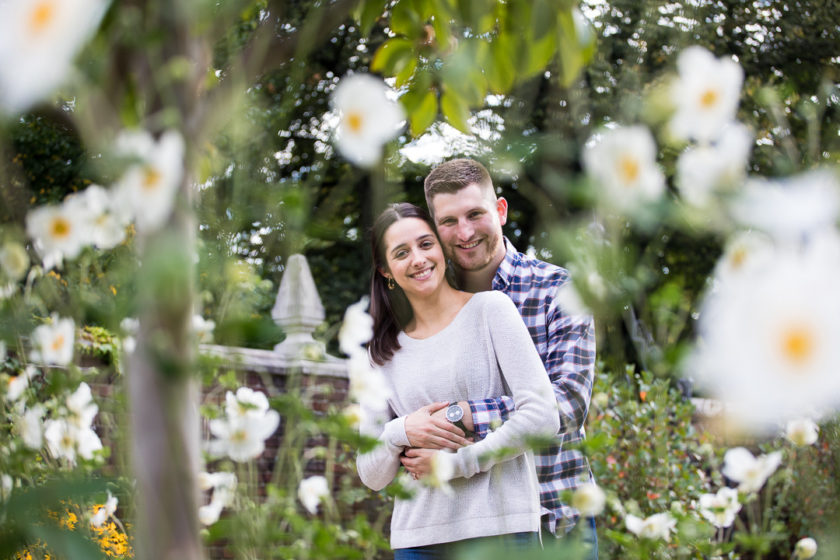 Snuggling engaged couple with white and yellow flowers